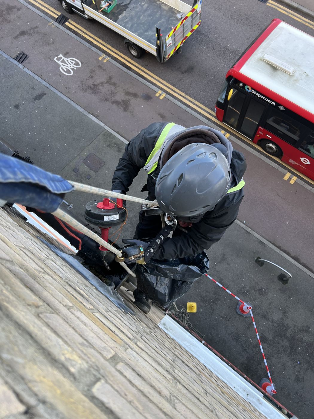 Technician clearing a high level gutter above a London street with the footway cordoned
