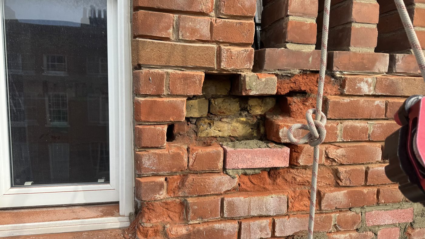 Severely weathered brickwork beside a window with bricks broken down and mortar joints failed